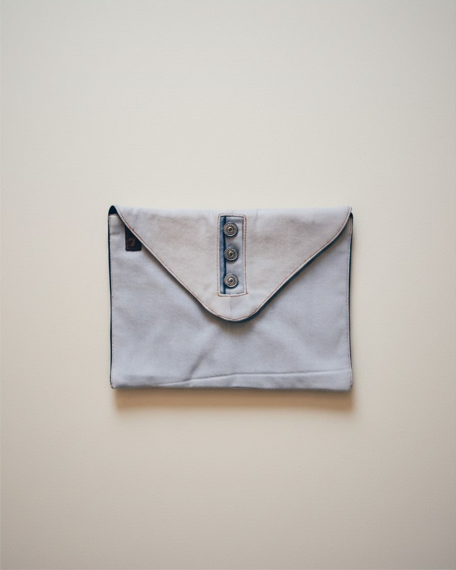 Hue Labs upcycled light blue denim envelope clutch with a three-button front closure on a neutral background.